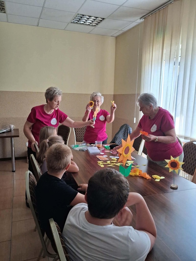 panie z KGW Ziemianki pokazujace dzieciom jak wykonać kwiat słonecznika z drewna i łyka