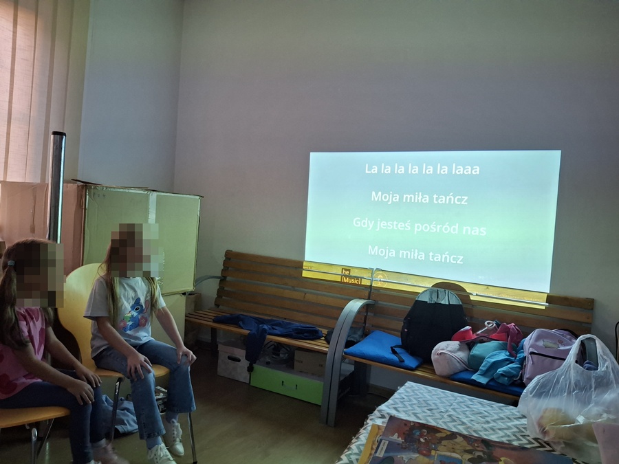 dziewczynka śpiewająca piosenke z tekstu wyświetlonego na ścianie przez rzutnik