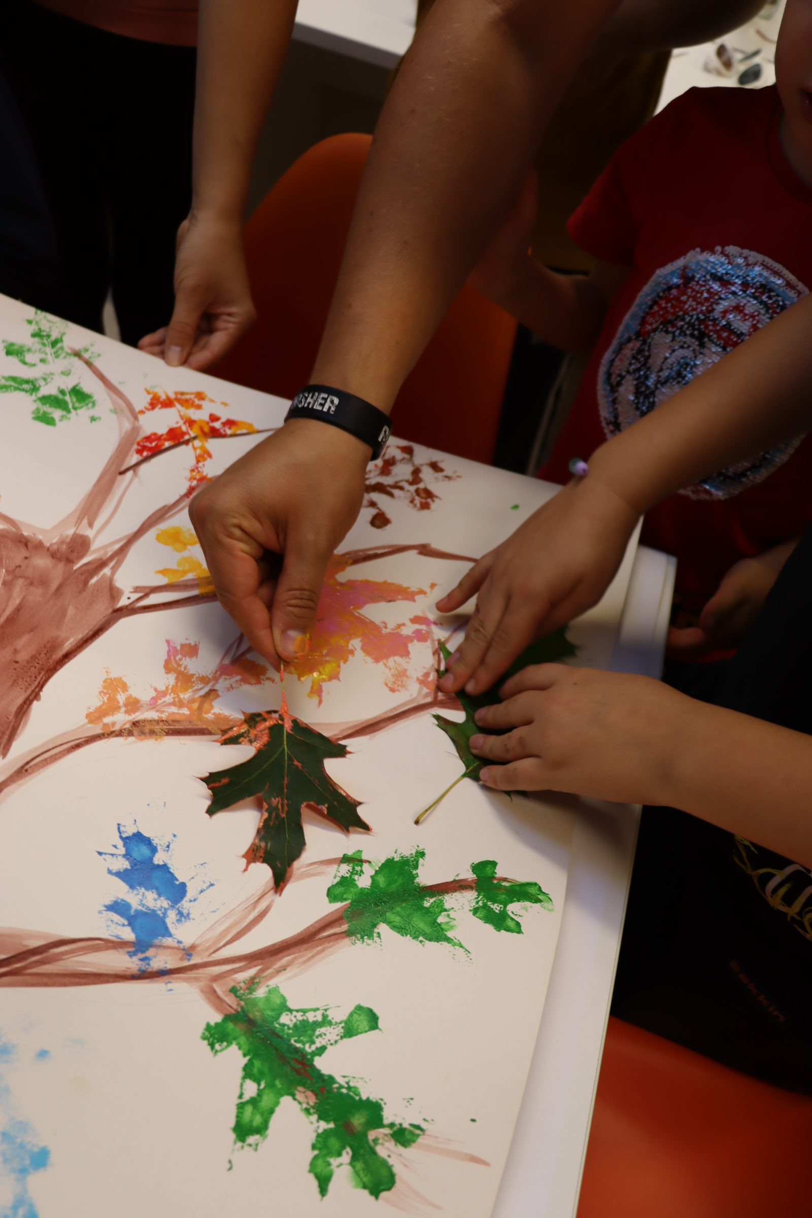 Dłonie, które odciskają pomalowane liście na namalowanym drzewie.