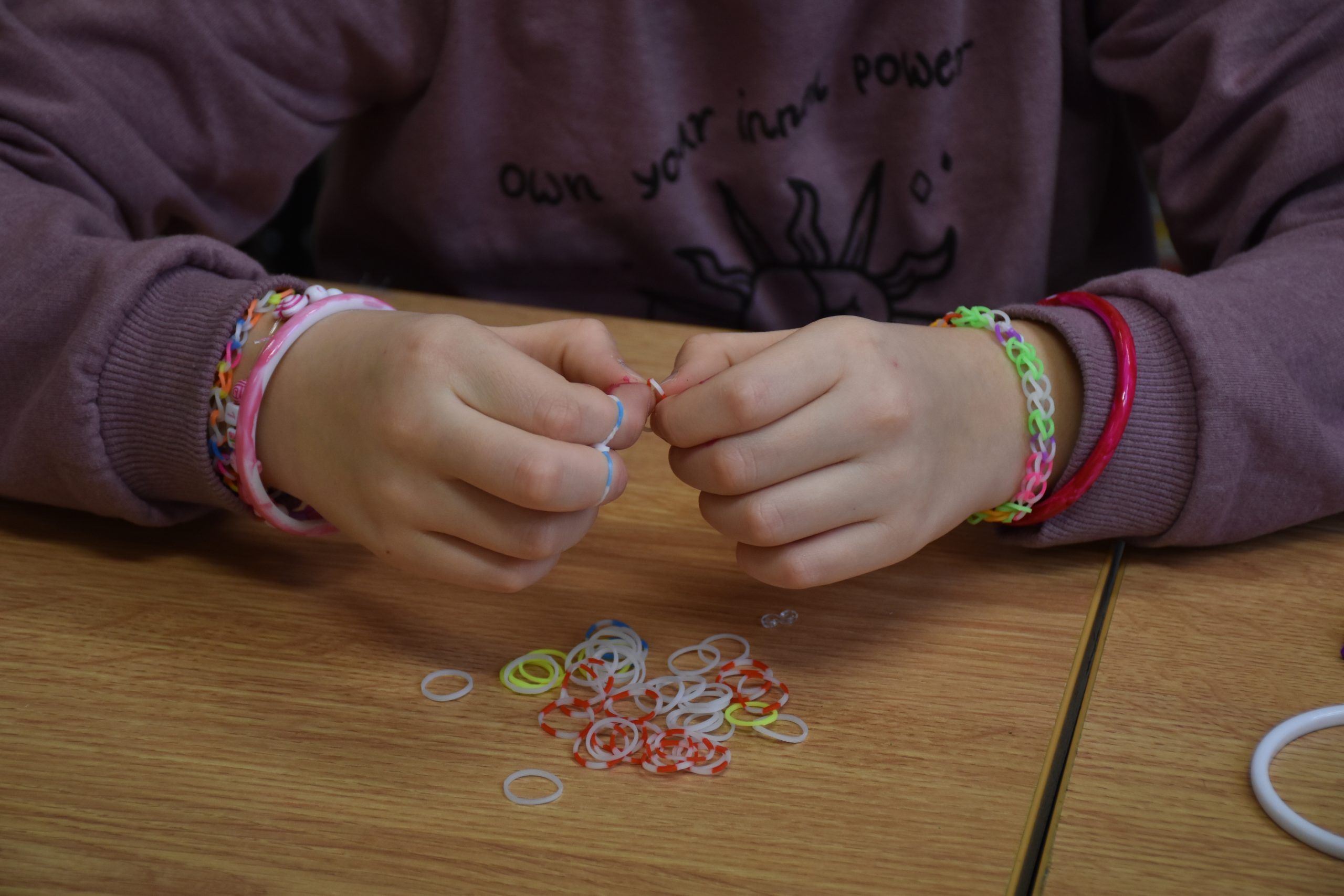 Tworzenie bransoletki - kolorowe zdjęcie przedstawiające dłonie podczas plecenie bransoletki.