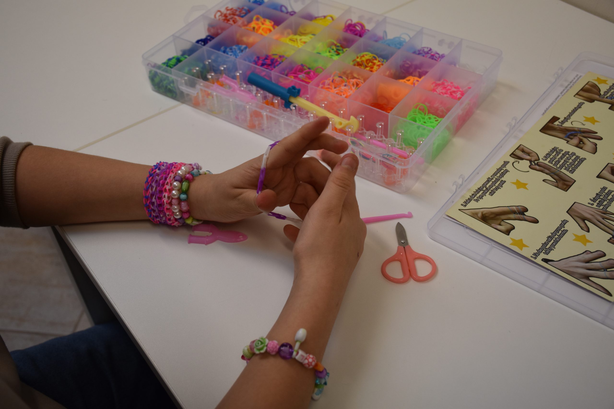Tworzenie bransoletki - kolorowe zdjęcie przedstawiające dłonie podczas plecenie bransoletki.