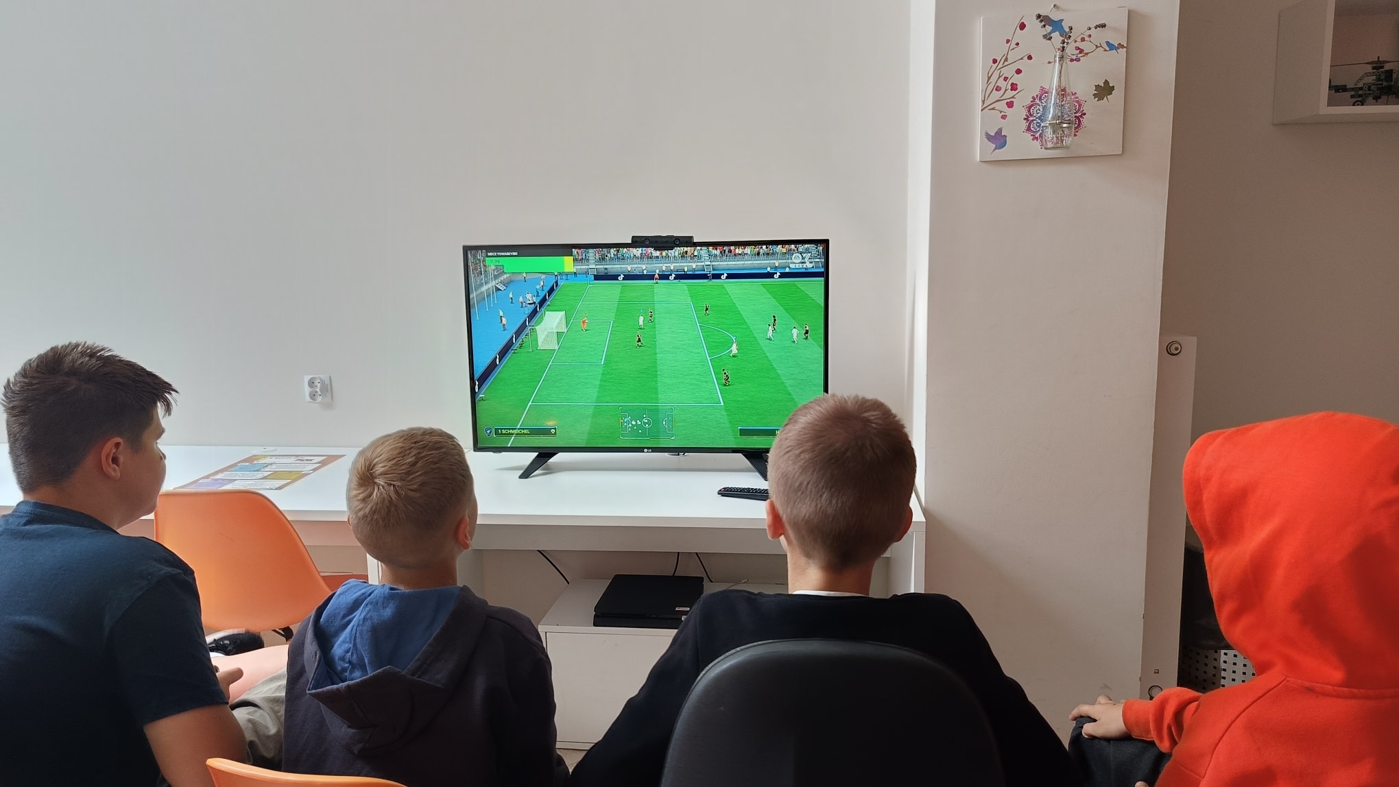 Dwaj chłopcy siedzący przy biurku z komputerem, na ekranie gra PS4