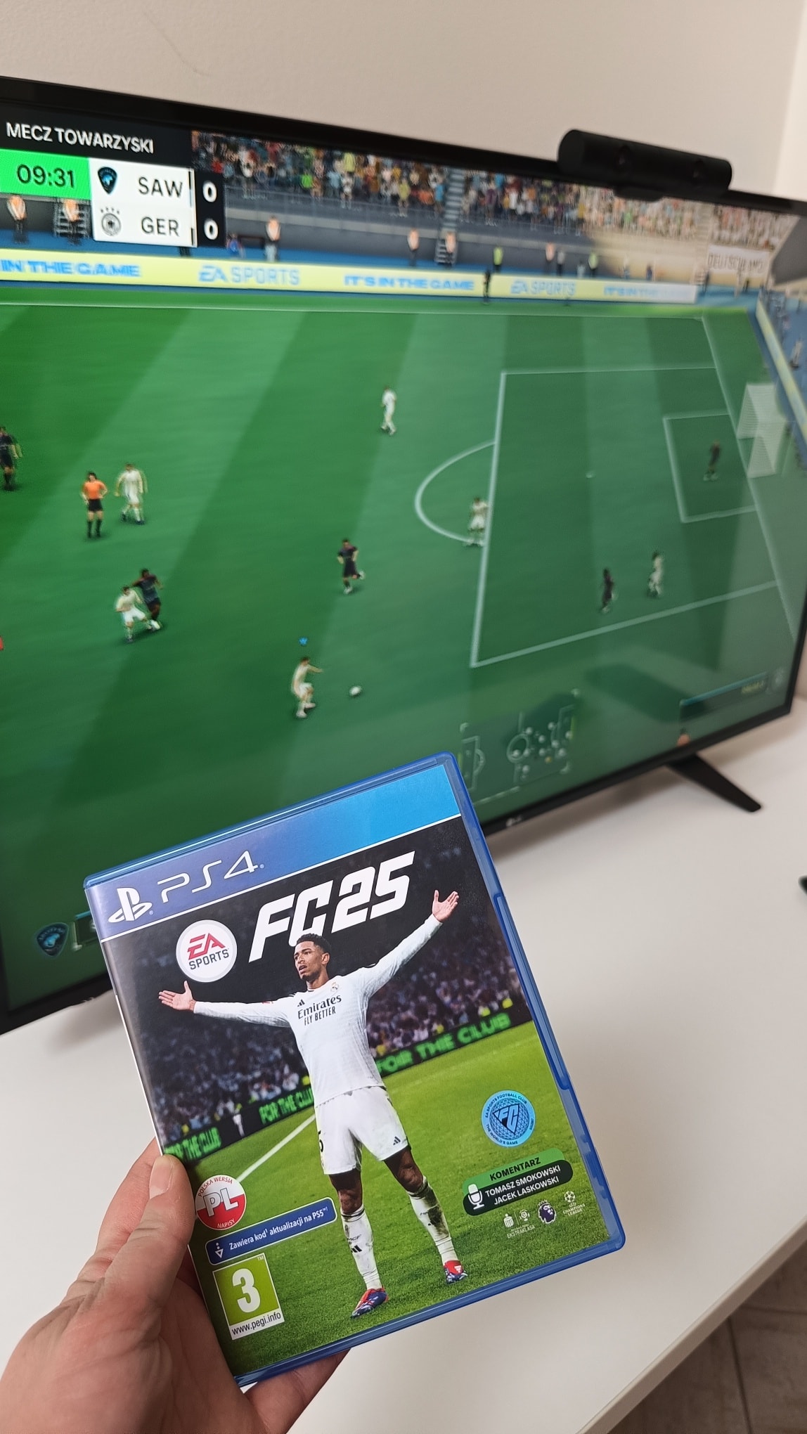 Zdjęcie dłoni trzymającej grę FC25, w tle ekran