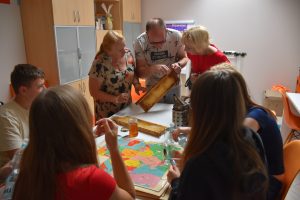 Grupa warsztatowa przy stole, mężczyzna pokazuje im plastry miodu na drewnie