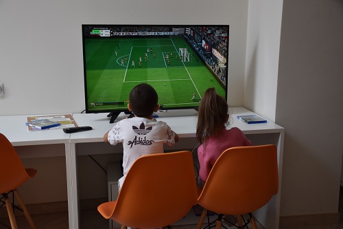 Dwójka dzieci przed monitorem, na ekranie gra piłkarska