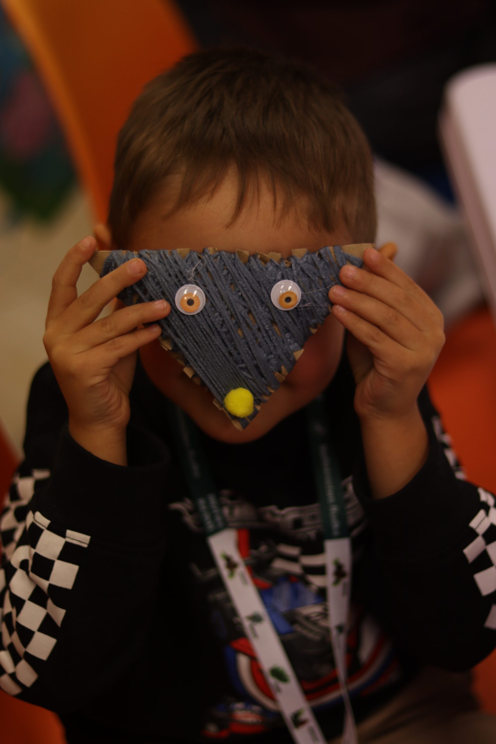 Dziecko zasłaniające twarz wykonaną pracą - wilkiem