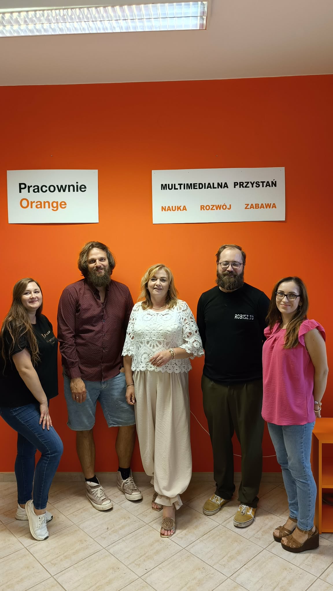 zdjęcie grupowe organizatorów z prowadzącymi na tle pomarańczowej ściany w Pracowni Orange