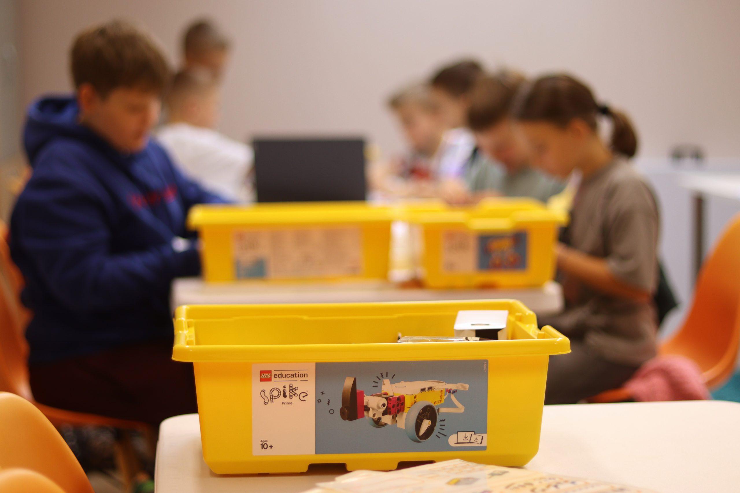 Na pierwszym planie pudełko LEGO, w tle uczestnicy zajęć