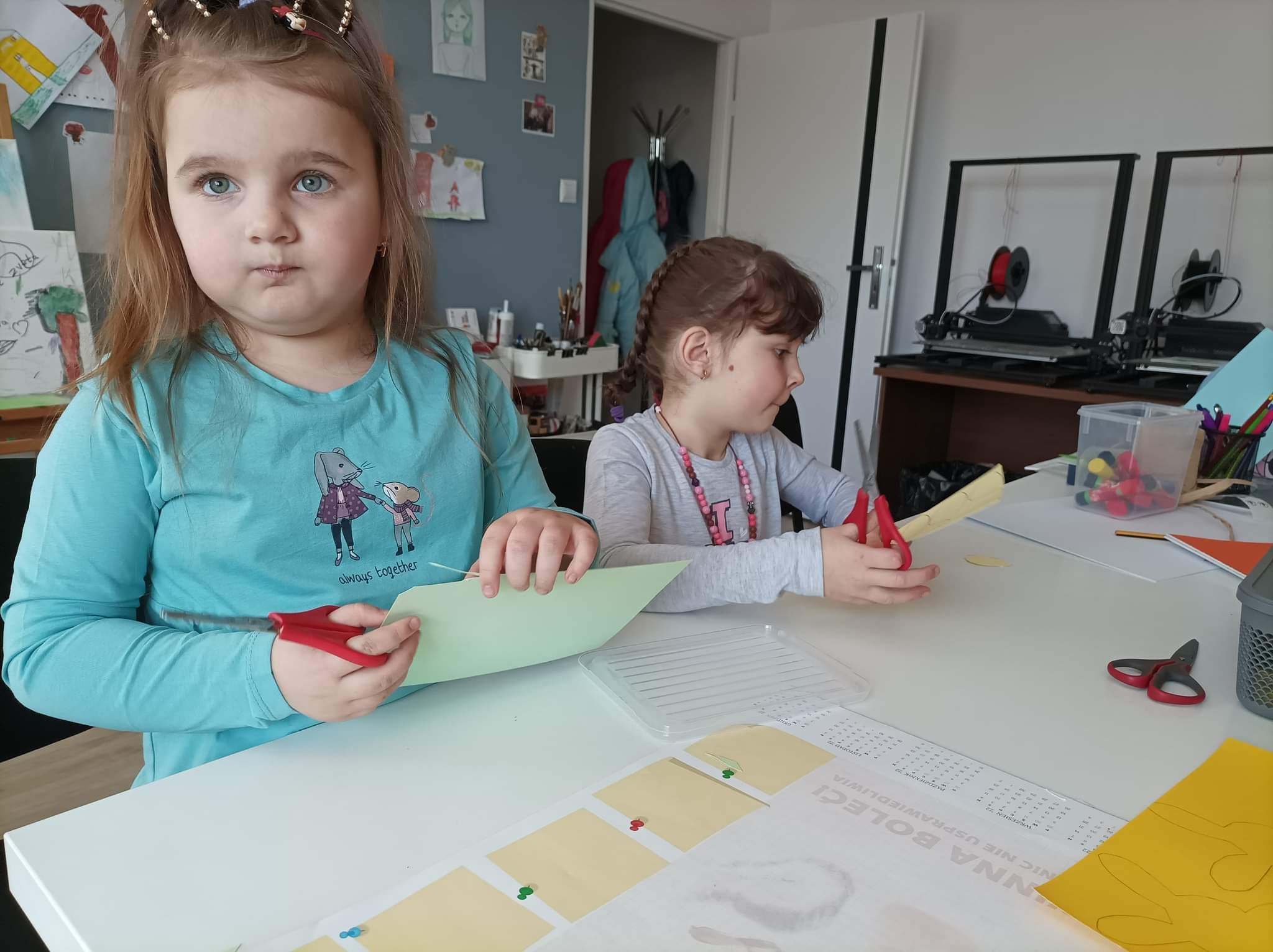 dzieci siedzą przy stole i wycinają z kolorowego papieru
