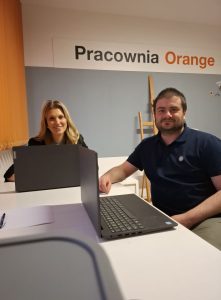 Dwie osoby siedzą przy laptopach i pozują do zdjęcia.