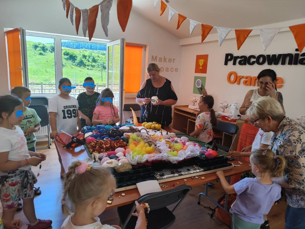 Grupa dzieci kończąca tworzenie ściany sensorycznej ułożonej na stole, pomaga im Pani prowadząca zajęcia