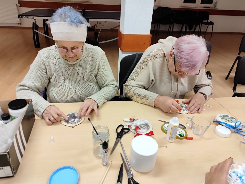 Dwie kobiety przyklejają świąteczne tło na bombkę z plexi.