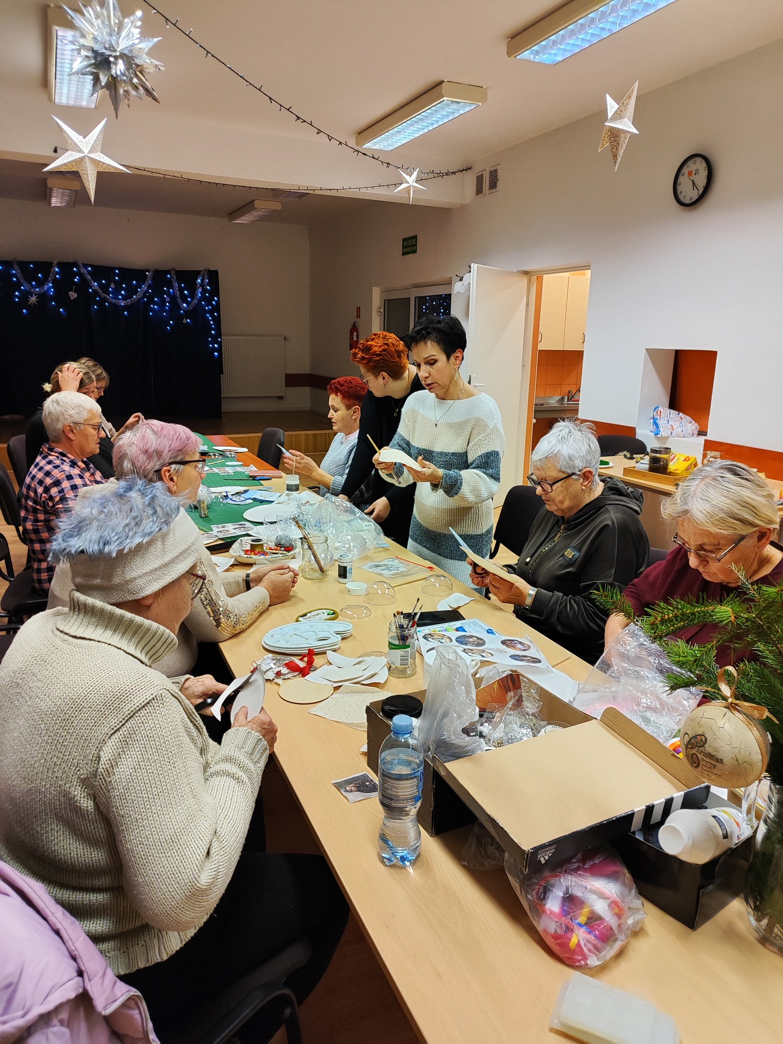 Grupa kobiet siedzi przy stole i tworzy świąteczne bombki.