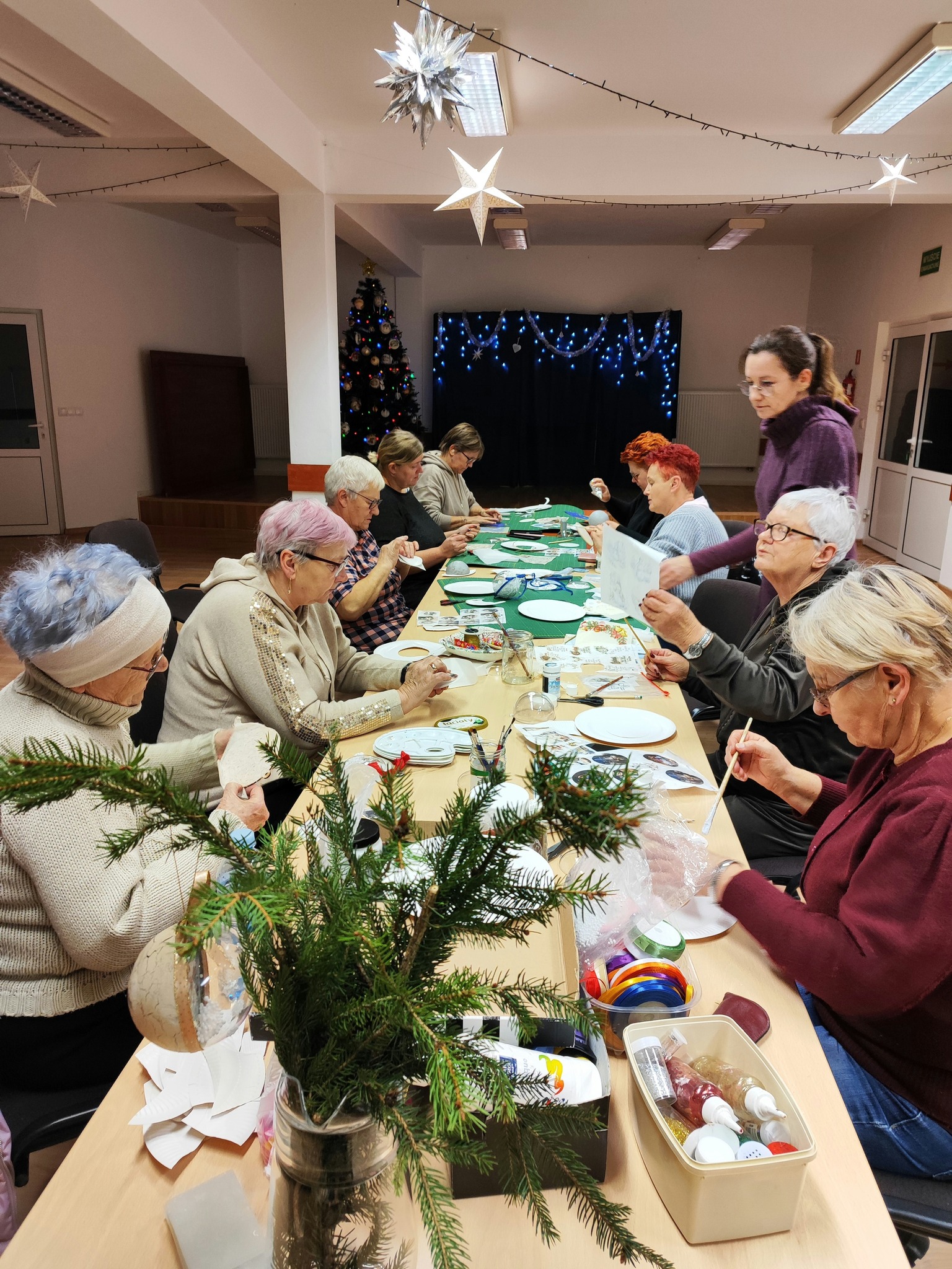 Grupa kobiet siedzi przy stole i tworzy świąteczne bombki.