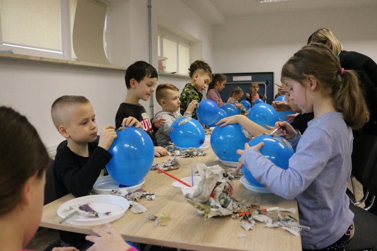 dzieci siedzą przy stole obklejają balony skrawkami gazet