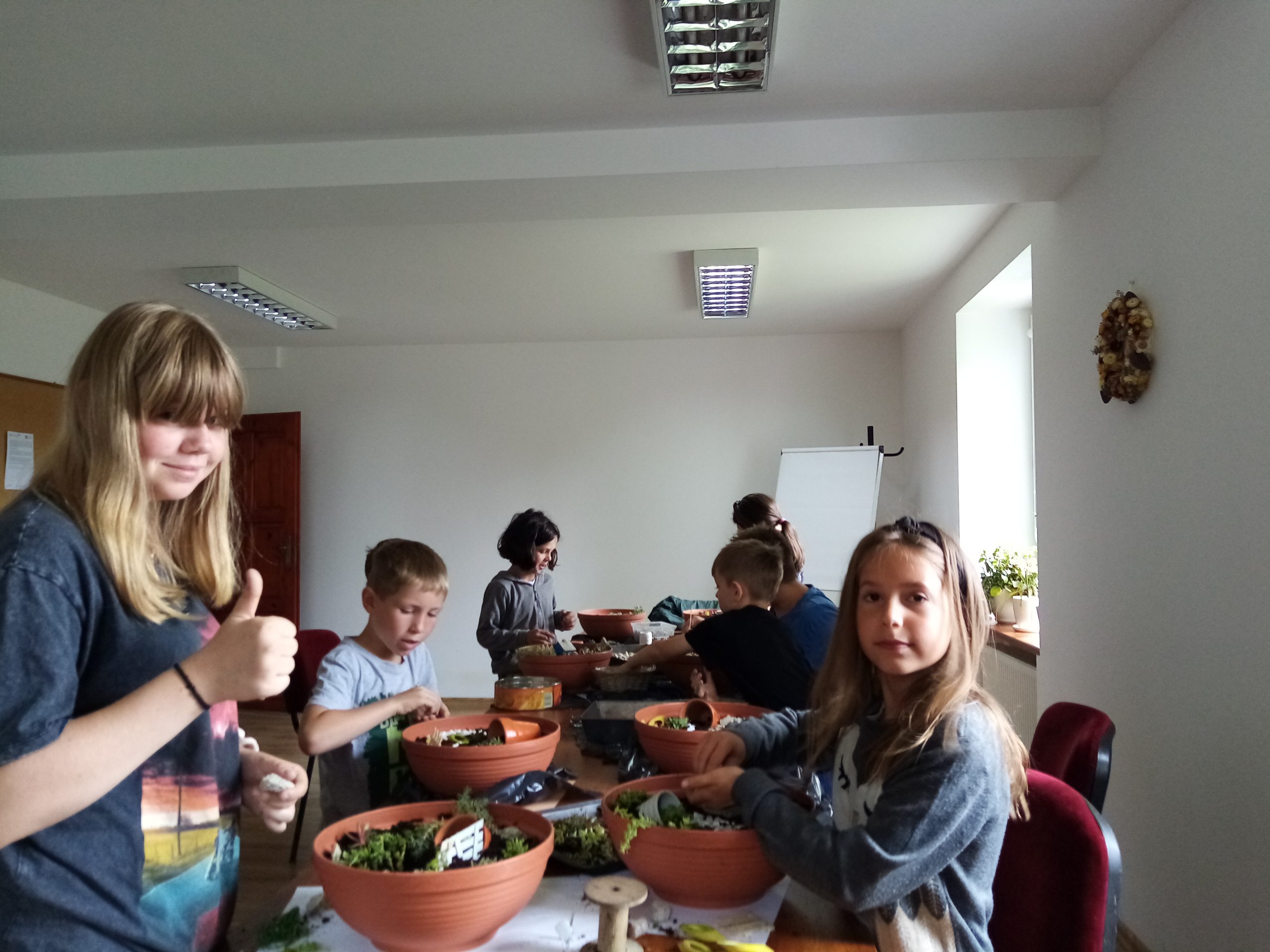 Zdjęcie. Dzieci siedzące przy stole podczas warsztatów tworzenia ogrodów wróżek.