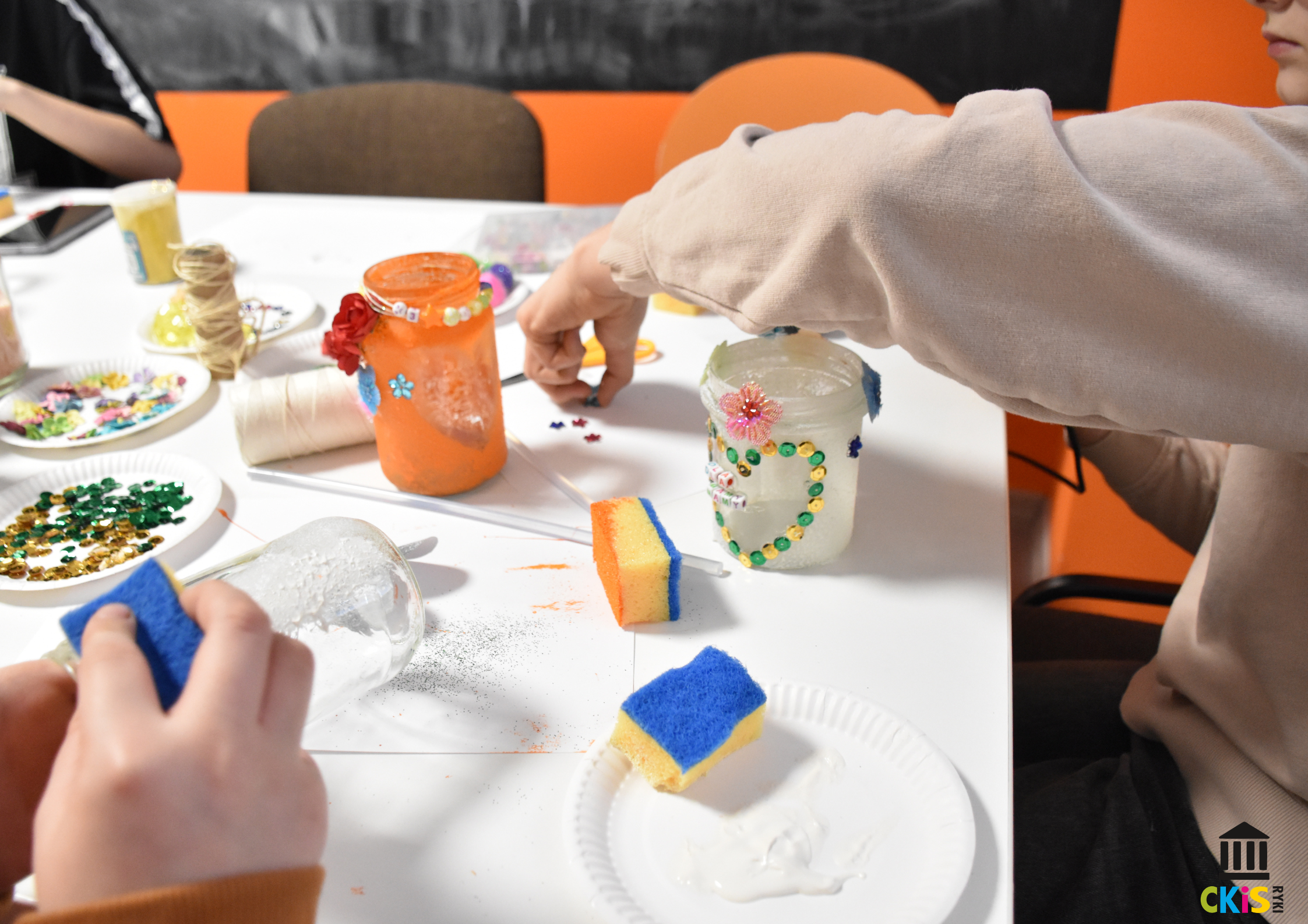 na zdjęciu widać dłonie dzieci, ozdabiają słoiczki, przyklejają ozdoby
