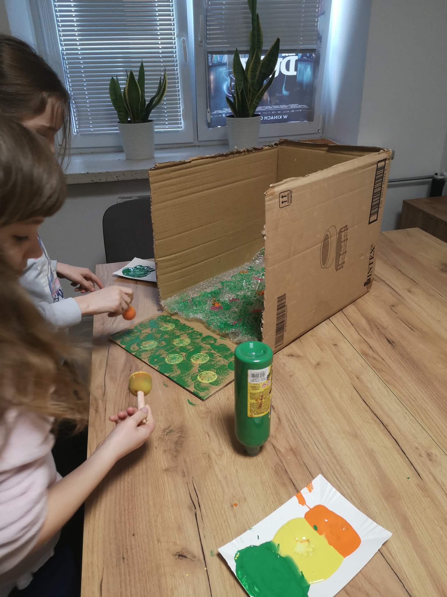 na zdjęciu widać dzieci malujących karton zielonymi farbami