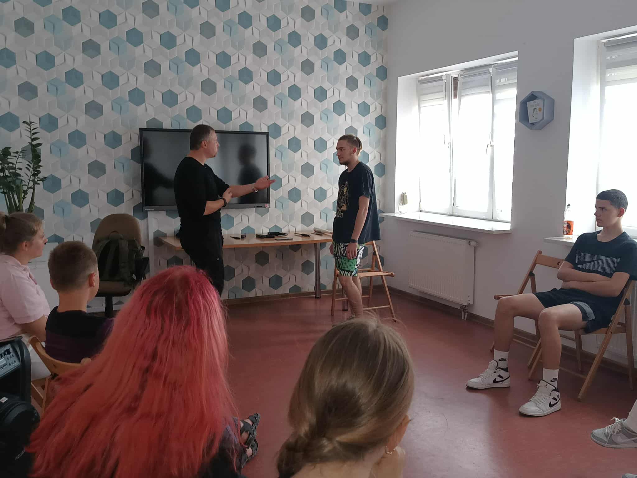 uczestnicy siedzą w kole na krzesełkach prowadzący z jednych chłopcem pokazuje podstawowe chwyty samoobrony