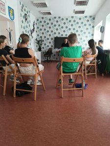 Młodzi ludzie siedzą w kręgu ,naprzeciwko stoi prowadzący kurs samoobrony