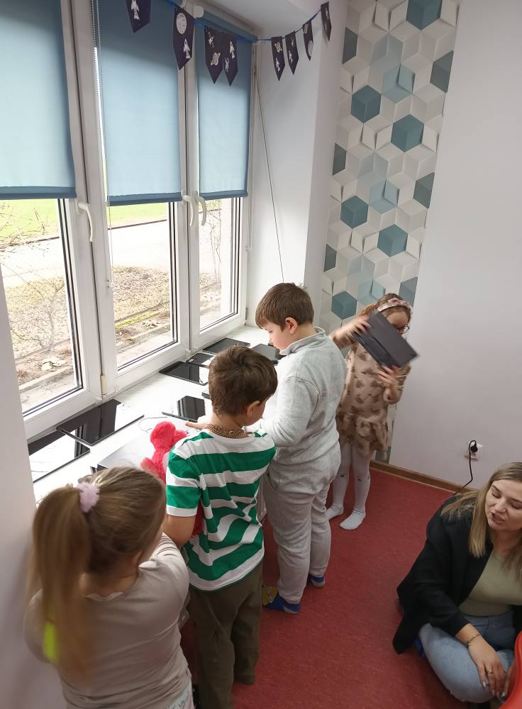 dzieci stoją przed oknem i wybierają tablety do zabawy