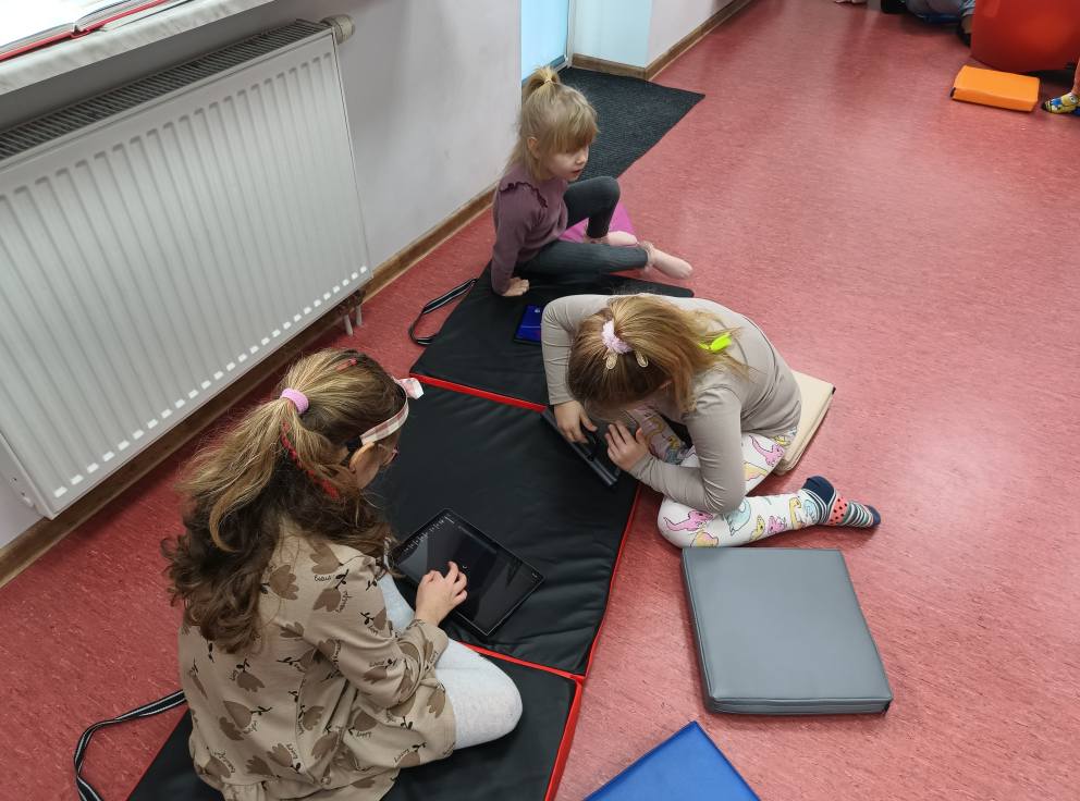 dzieci siedzą na materacu i obsługują tablety