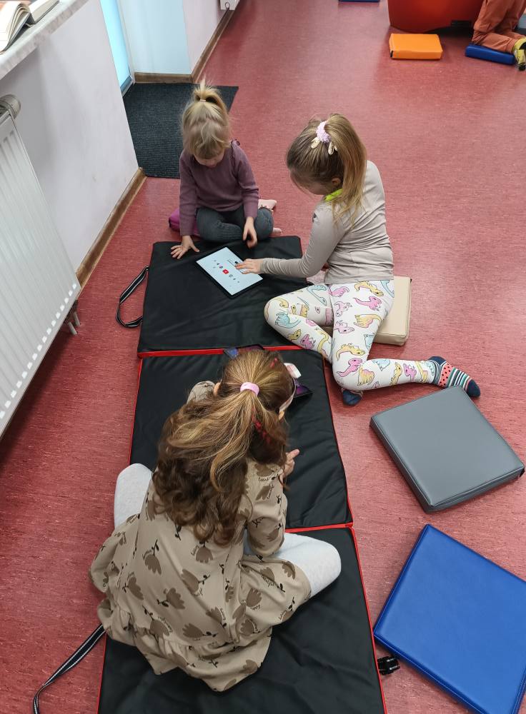 dzieci siedzą na materacu i obsługują tablety