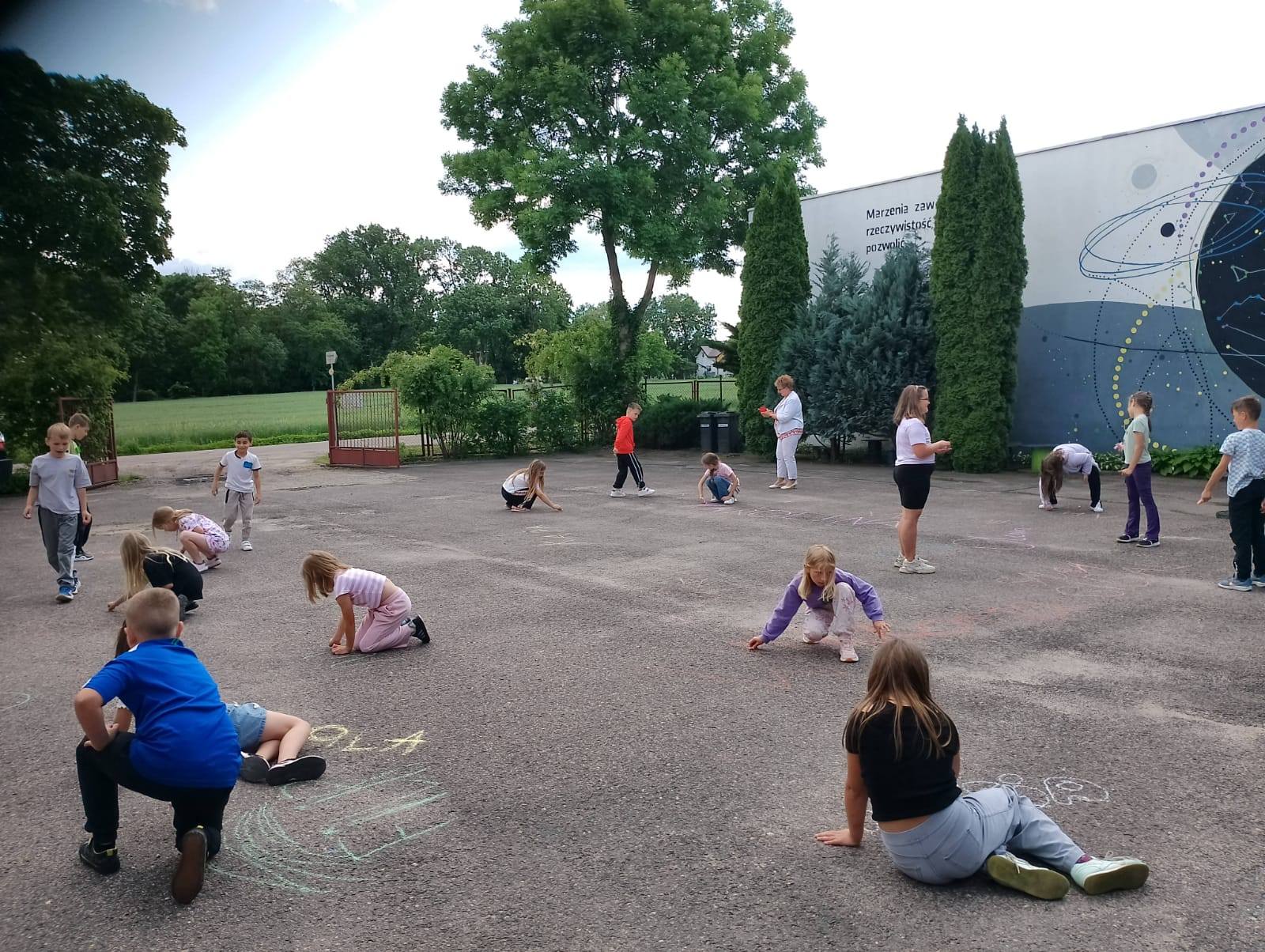 Dzieci na placu Pracowni na pamiątkę piszą kredą swoje imiona