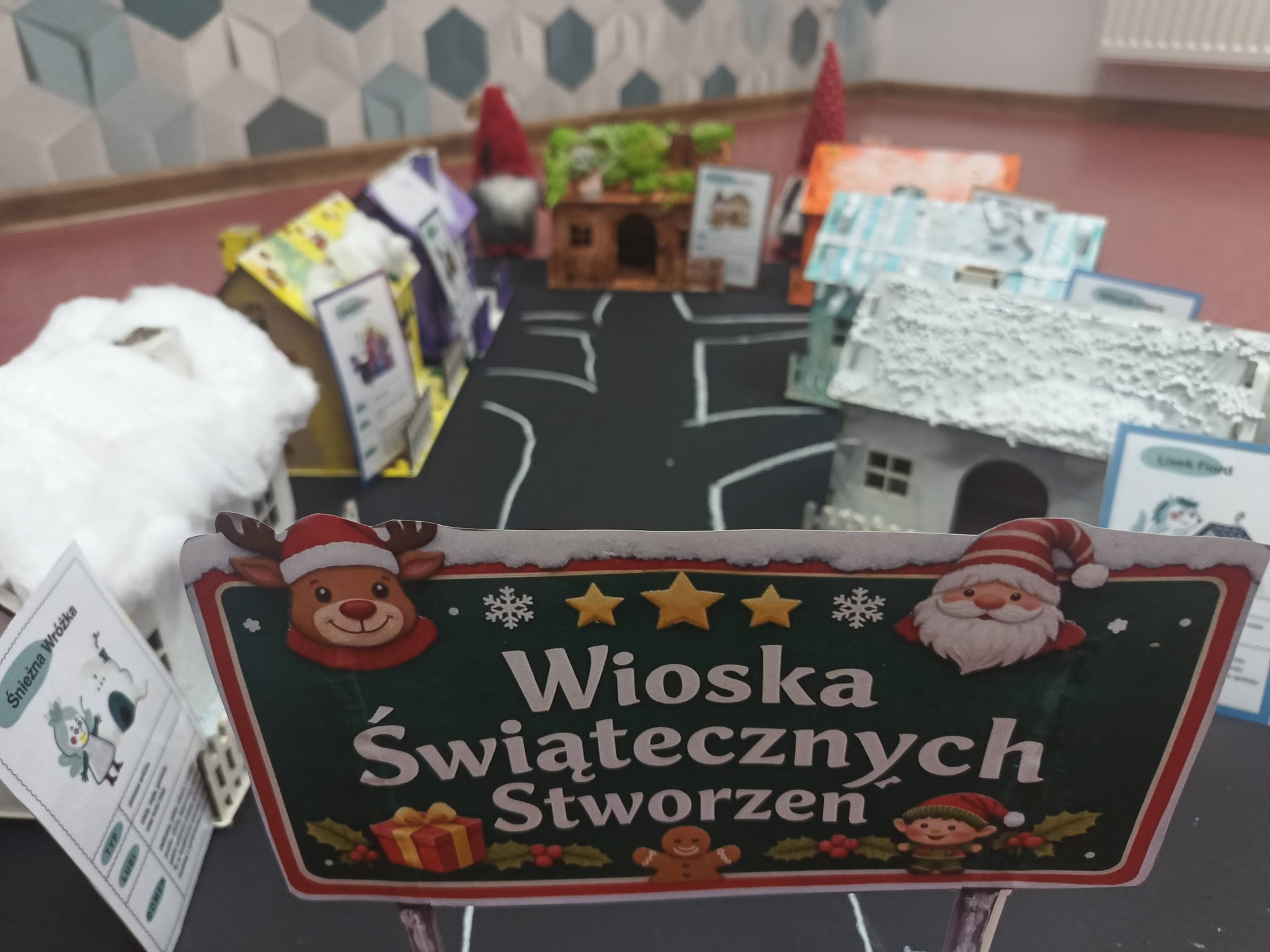 prace dzieci, domku stojące na narysowanej drodze z napisem wioska świątecznych stworzeń