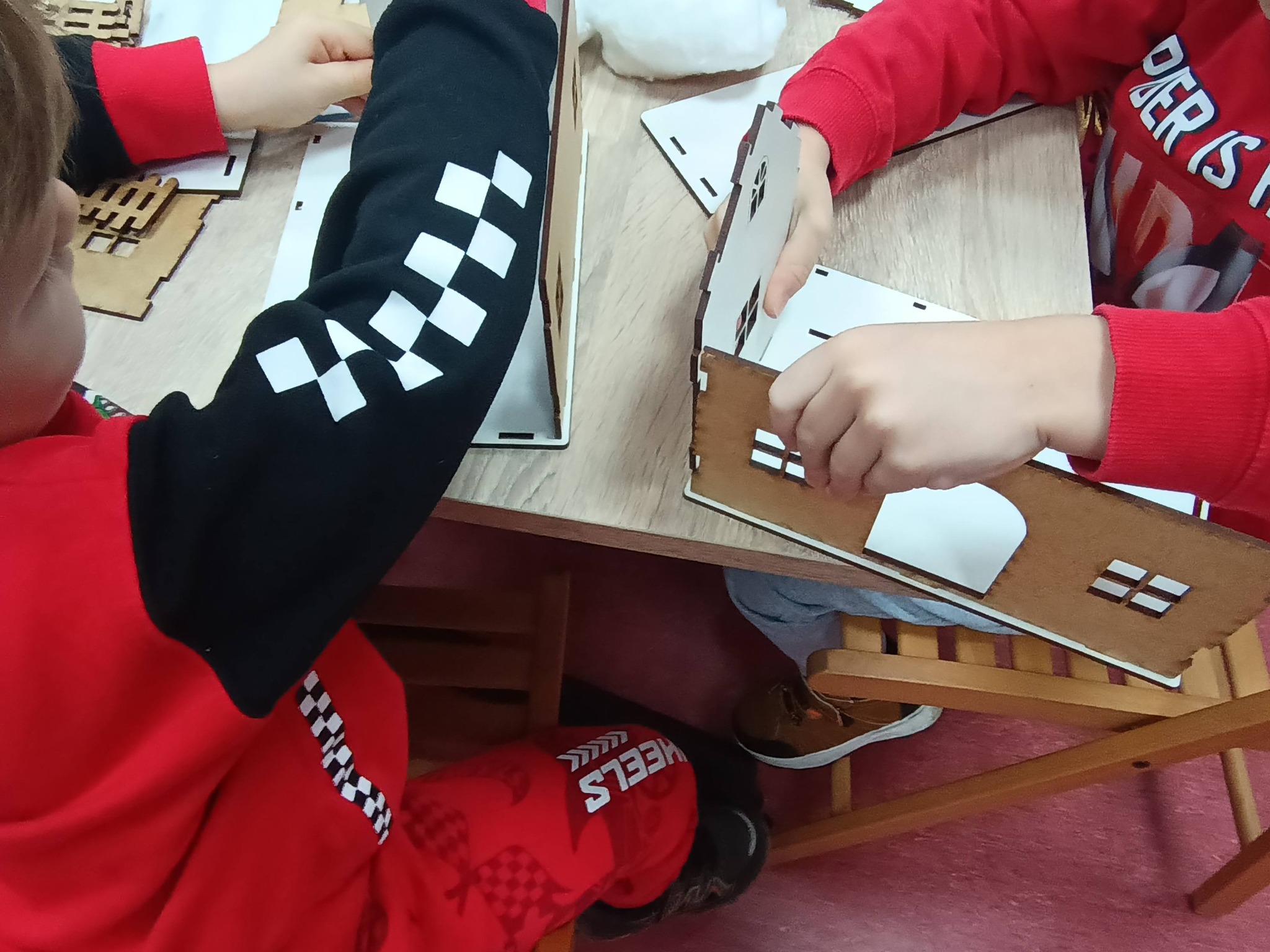 dzieci składajace domki z płyty wyciętej na ploterze laserowym