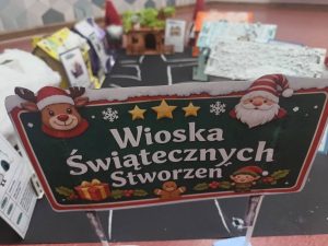 znak Drogowy Wioska Świątecznych Stworzeń a w tle domki , prace dzieci