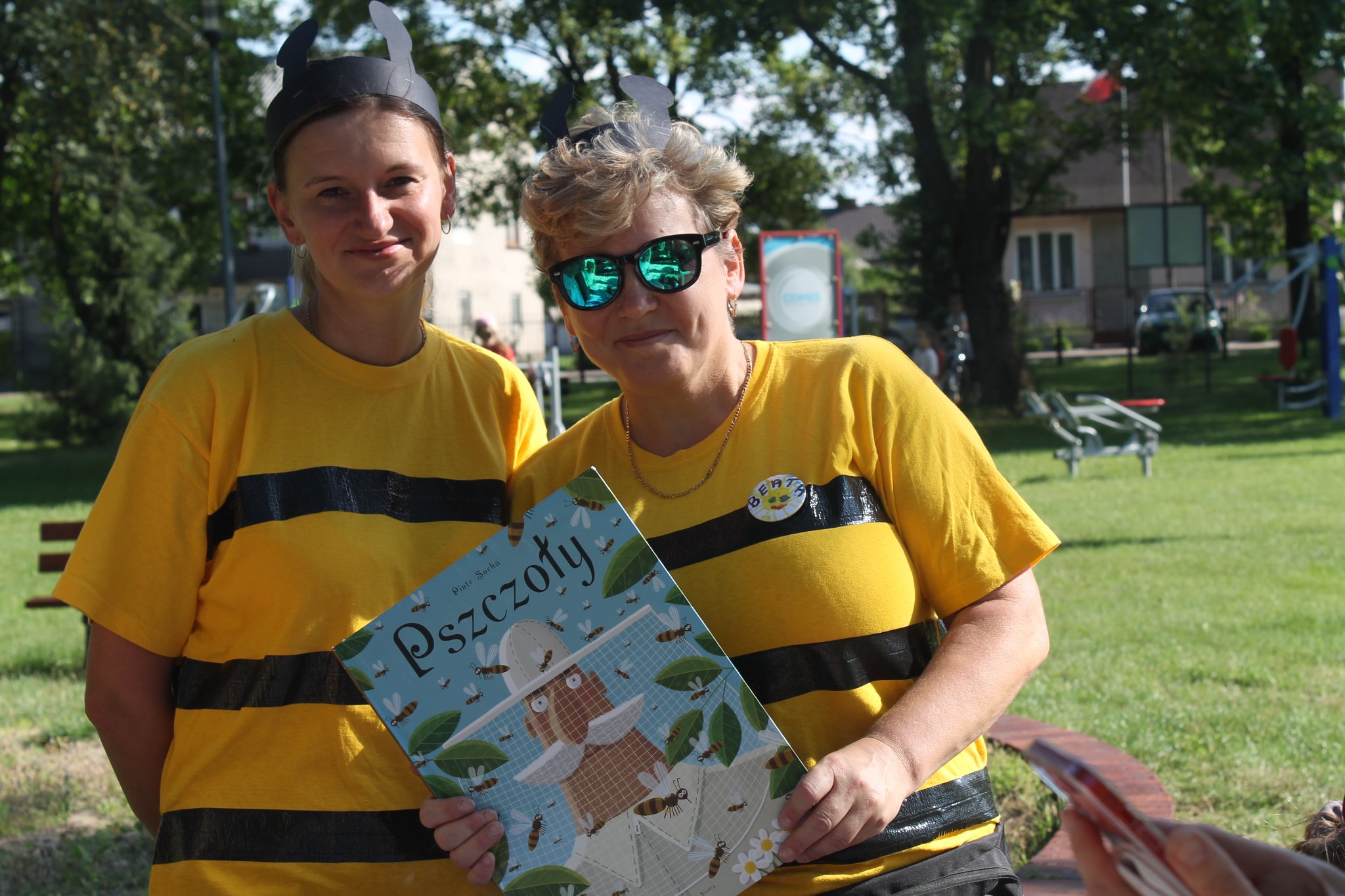 Dwie kobiety w żółtych t-shirtach, trzymające książkę o pszczołach.