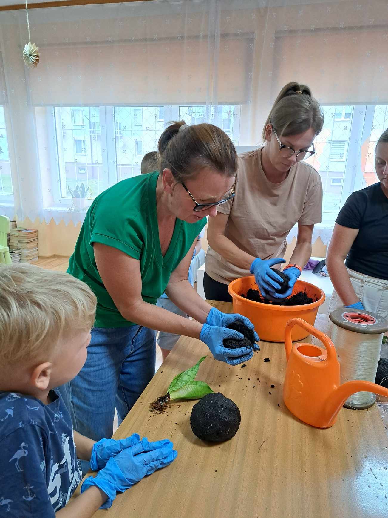 Kilka kobiet i chłopiec nabierają ziemię do formowania kokedamy.