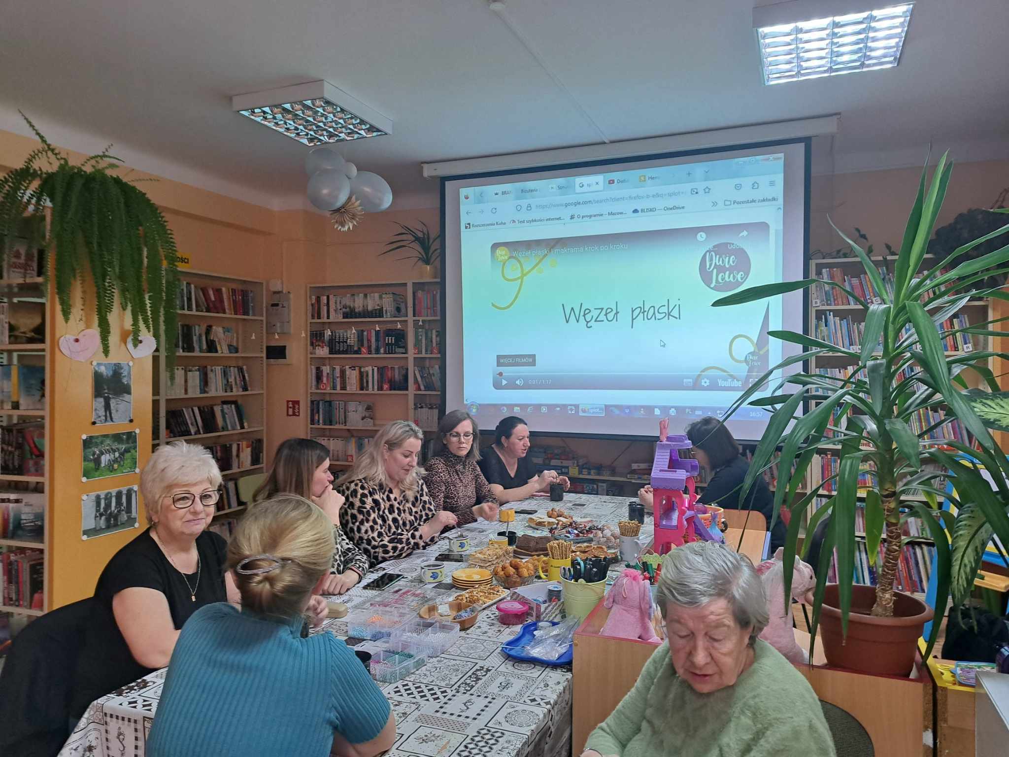 Przy stole siedzą panie i plotą makramowe sploty.