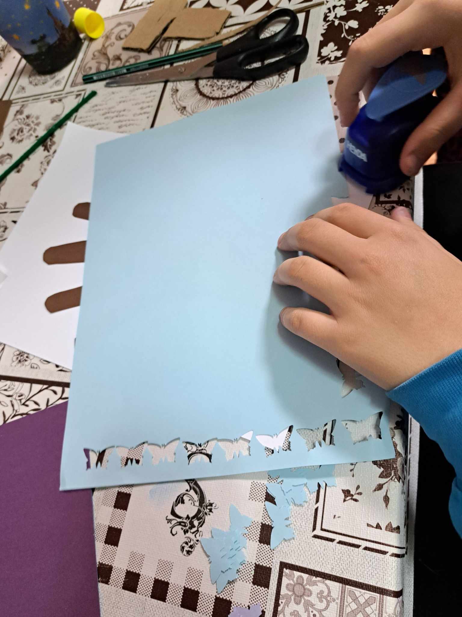 Kadr zdjęcia pokazujący ręce osoby wycinającej motyle z papieru.