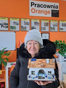 Pani trzyma w rękach drewniany domek, ozdobiony światecznie.