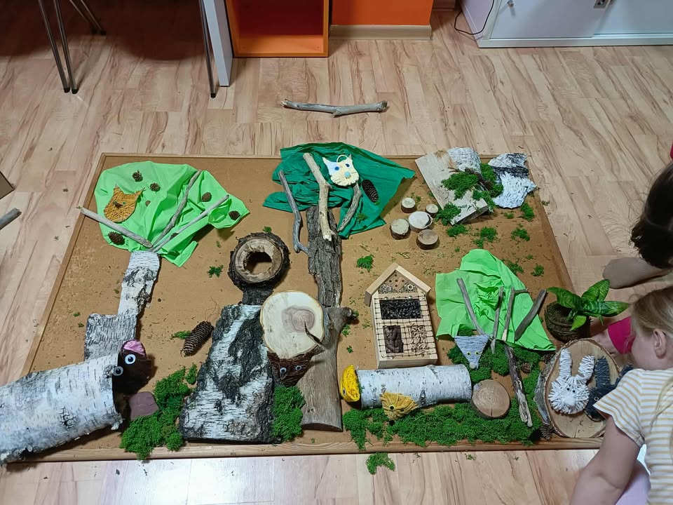 Makieta zawierająca zwierzątka z włóczki z elementami naturalnymi (kora, szyszki, kamyki, patyki itp.)