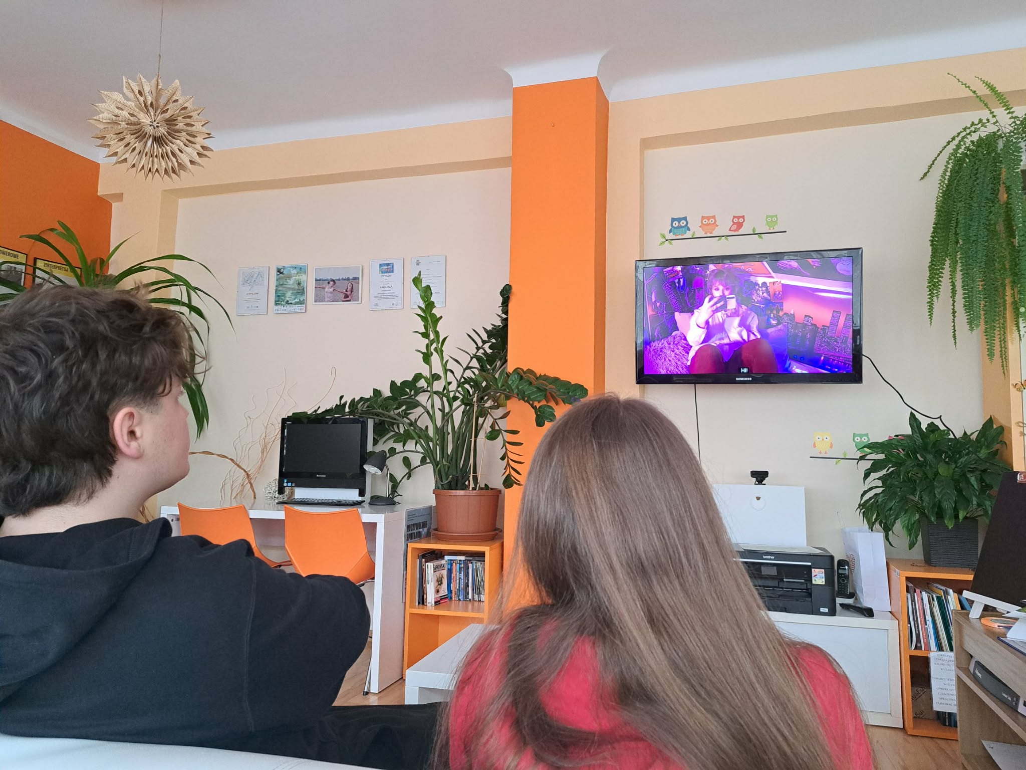 Młodzi ludzie siedzą przed telewizorem i oglądają film.