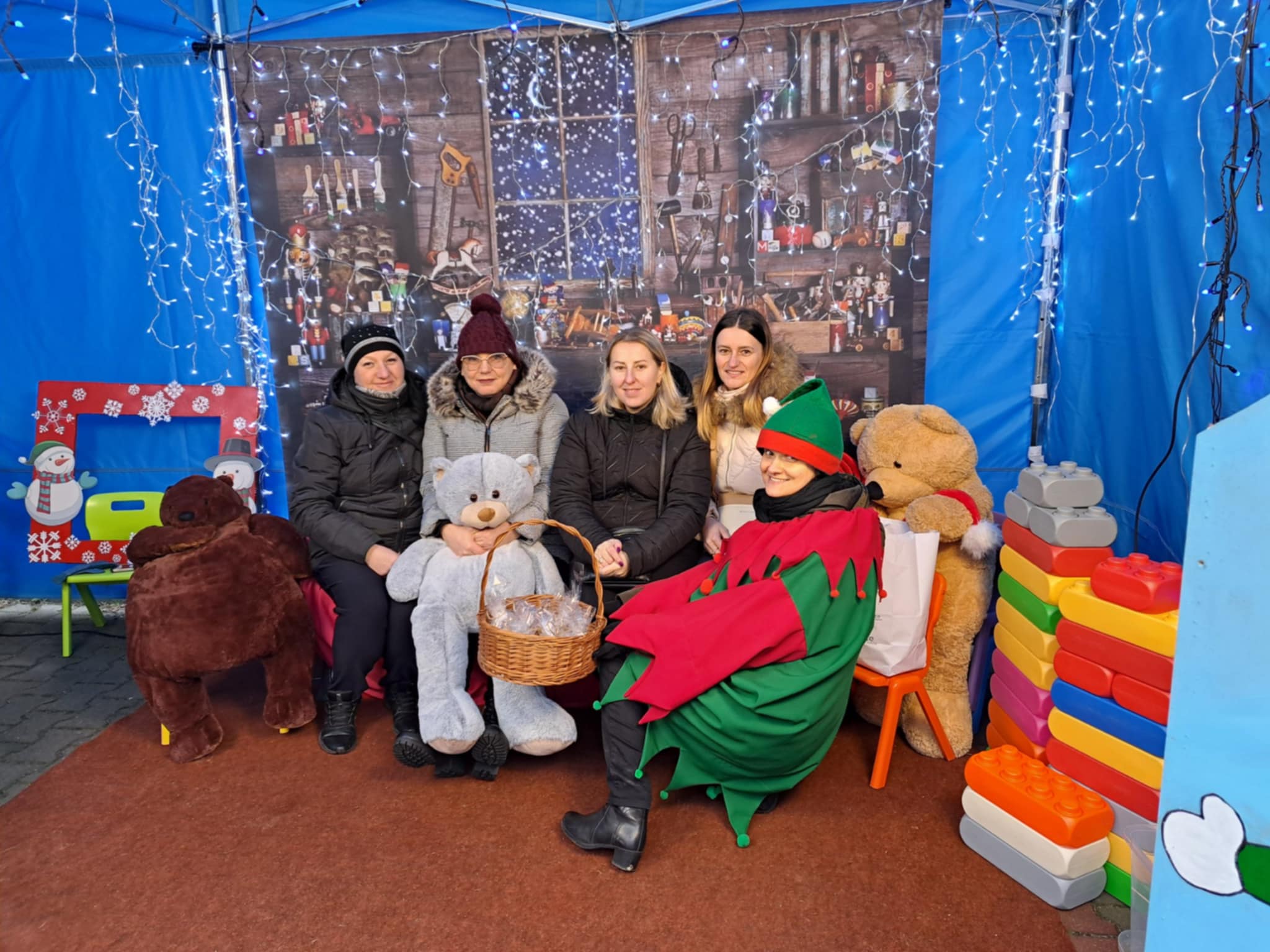 Cztery kobiety pozujące na tle świątecznej scenerii oraz elfem.