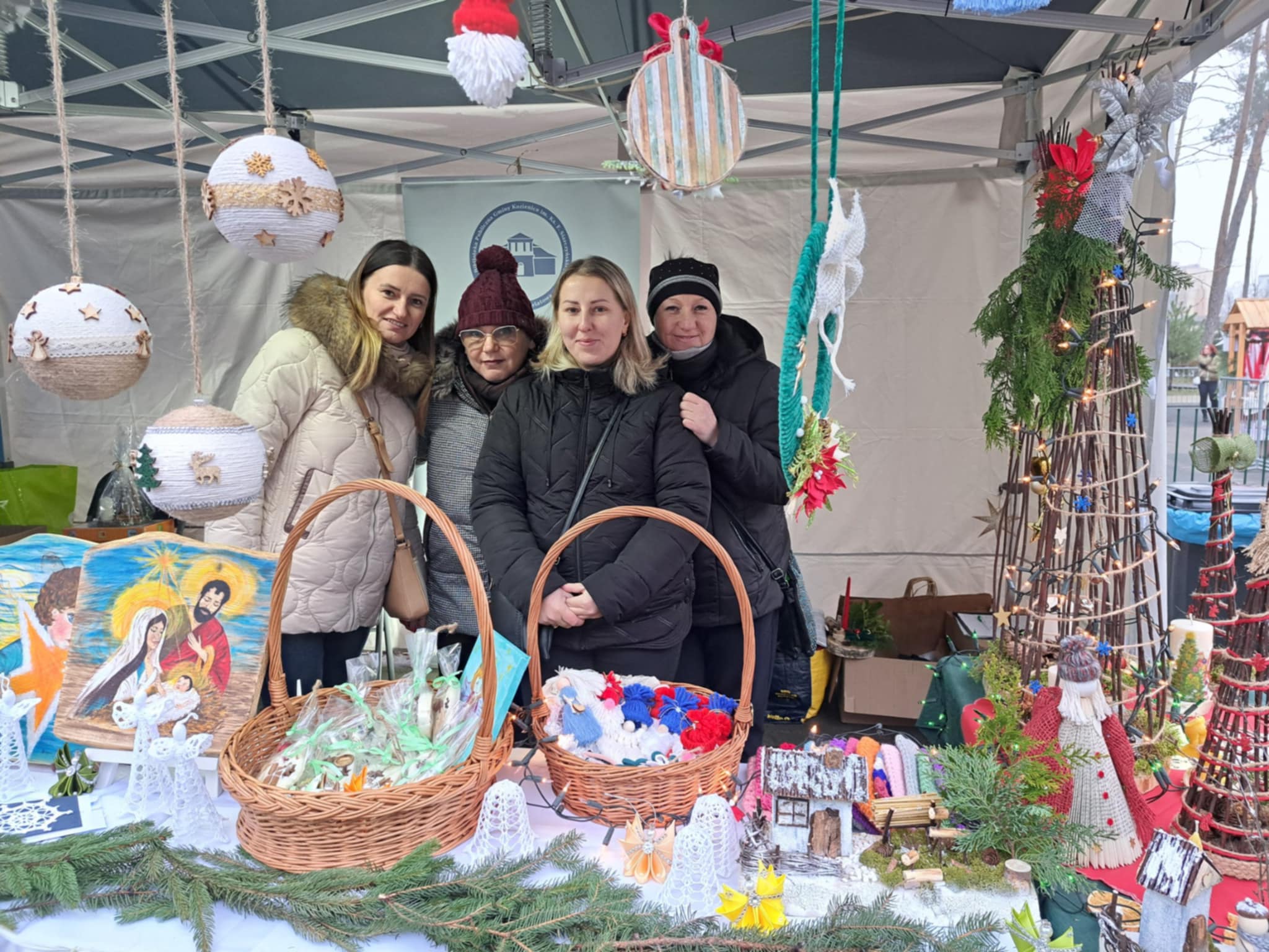 Cztery panie stoja pod namiotem. za stołem z dekoracjami światecznymi.