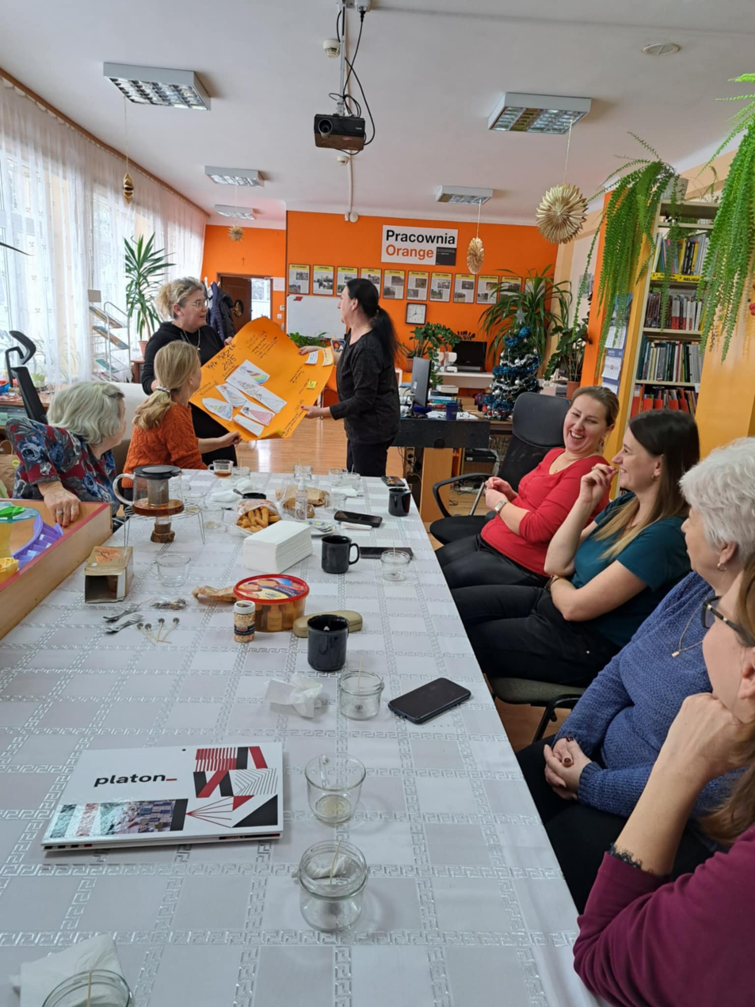 Grupa kobiet siedzi przy stole i spogląda na plakat.