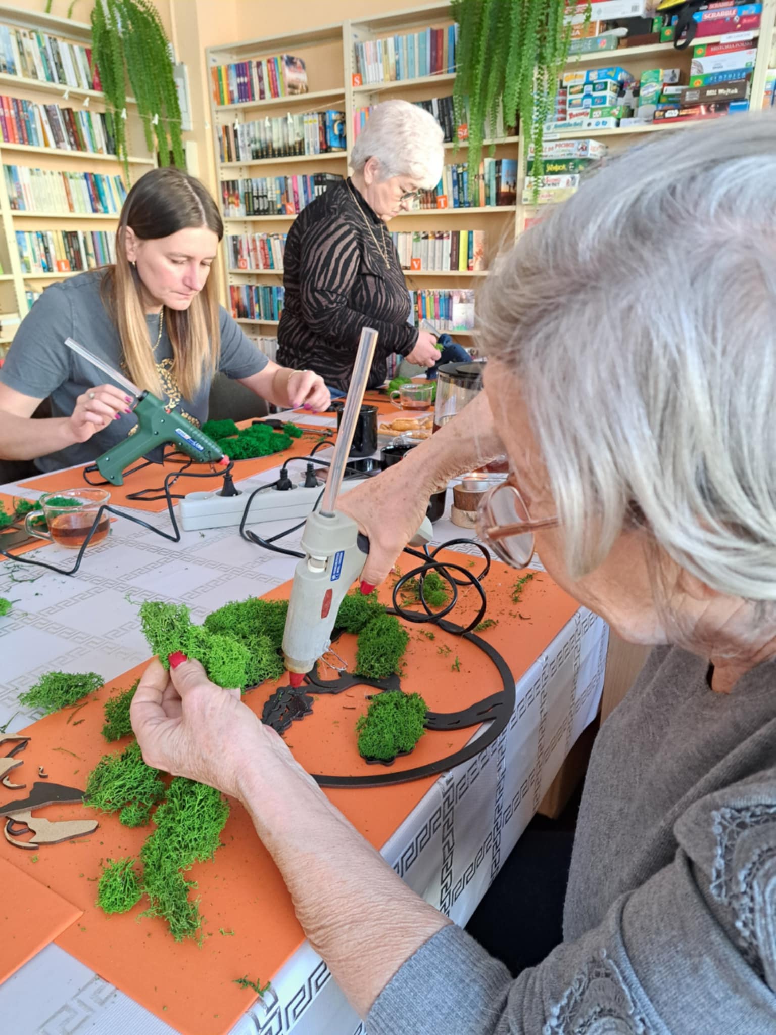 Kobiety przy stole przyklejają mech klejem na gorąco.
