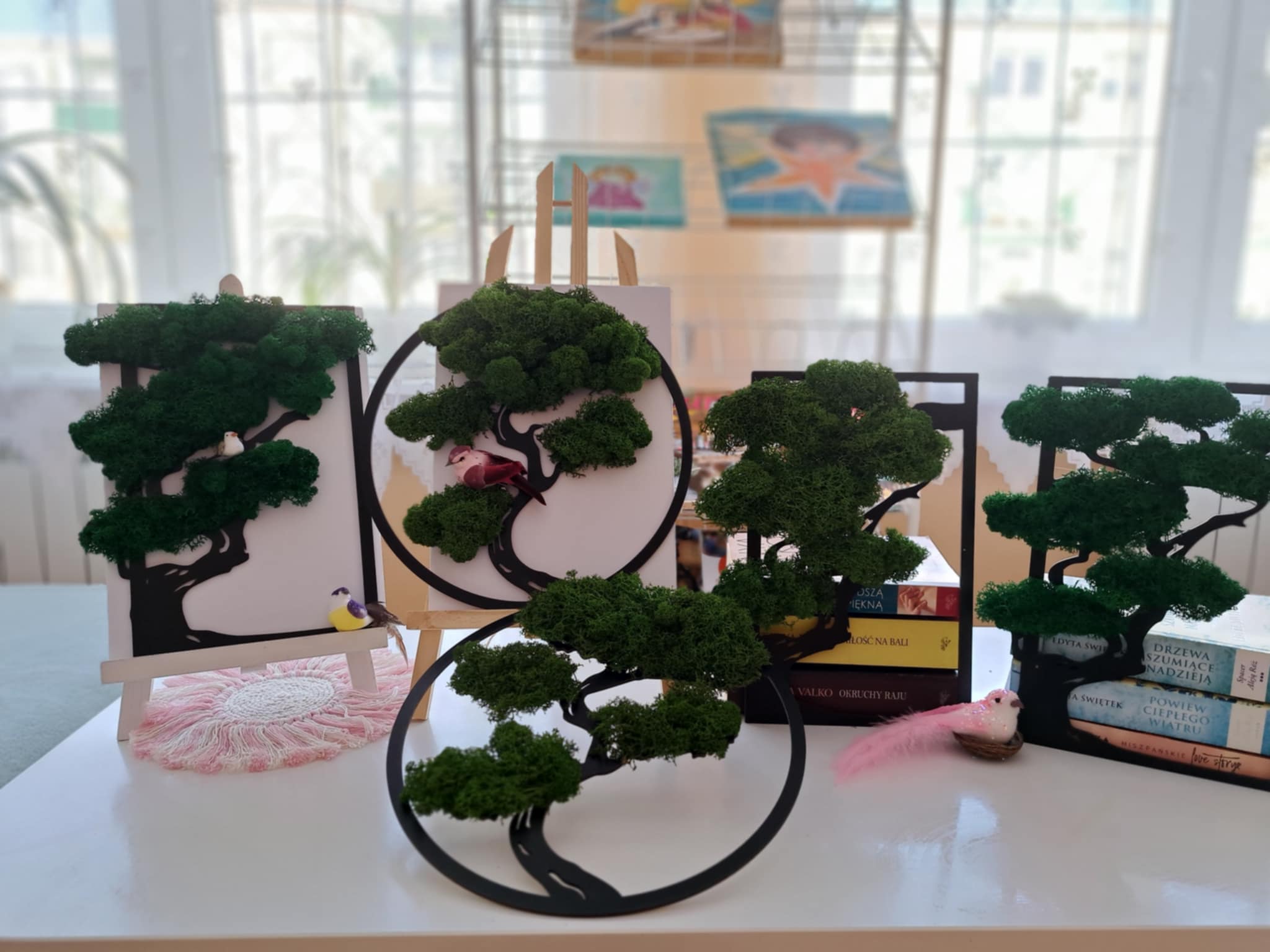Na białej ławie stoją dekoracje drzewek z mchem.