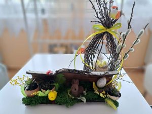 Na białej ławie stoi świąteczny stroik