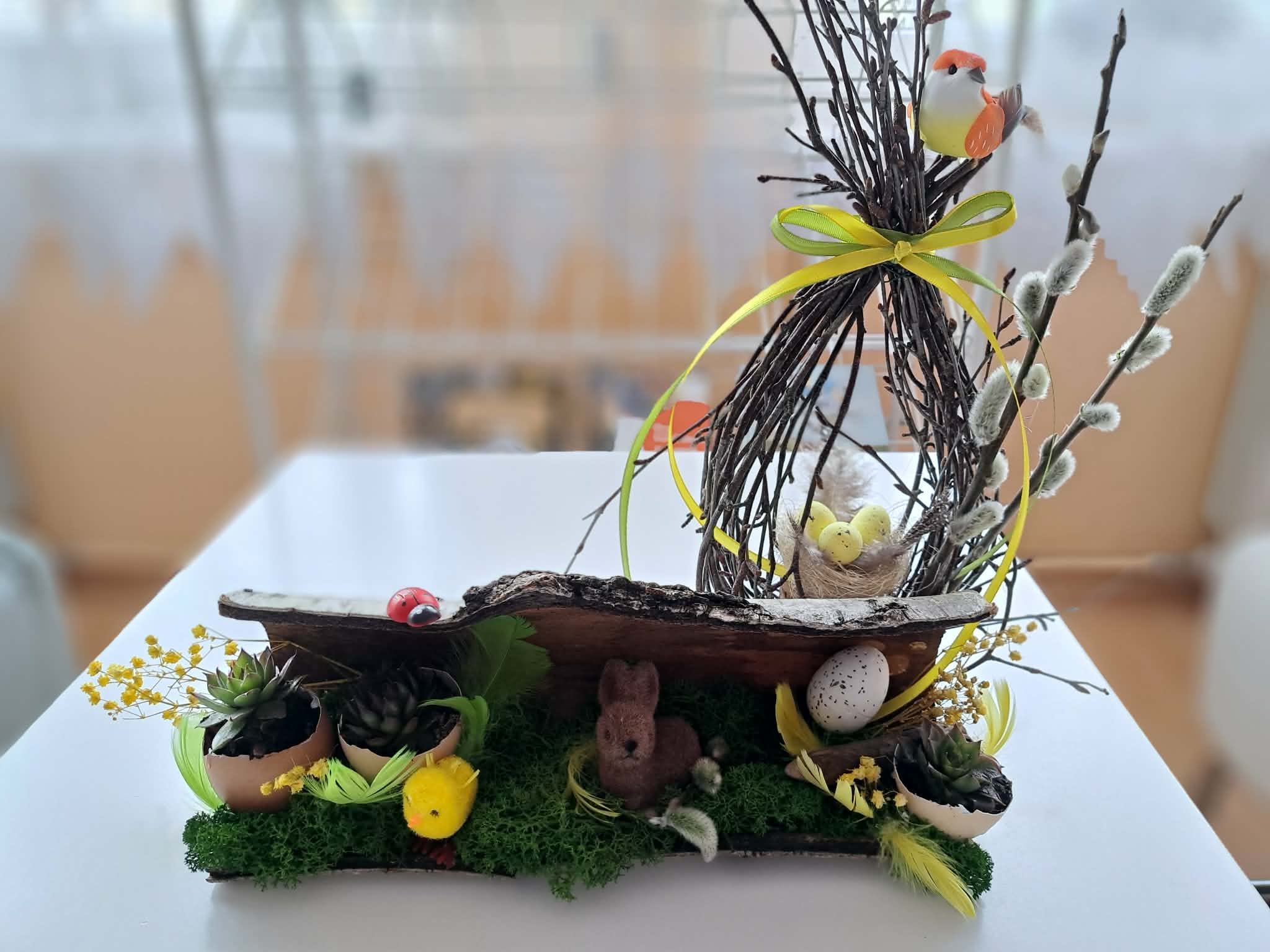 Na białej ławie stoi świąteczny stroik