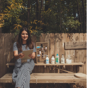 Kobieta siedzi na ławce a obok niej stoją różnorakie pojemniczki.