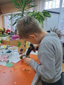 Chłopiec wykonuje świąteczny stroik, trzyma pistolet do kleju na gorąco.