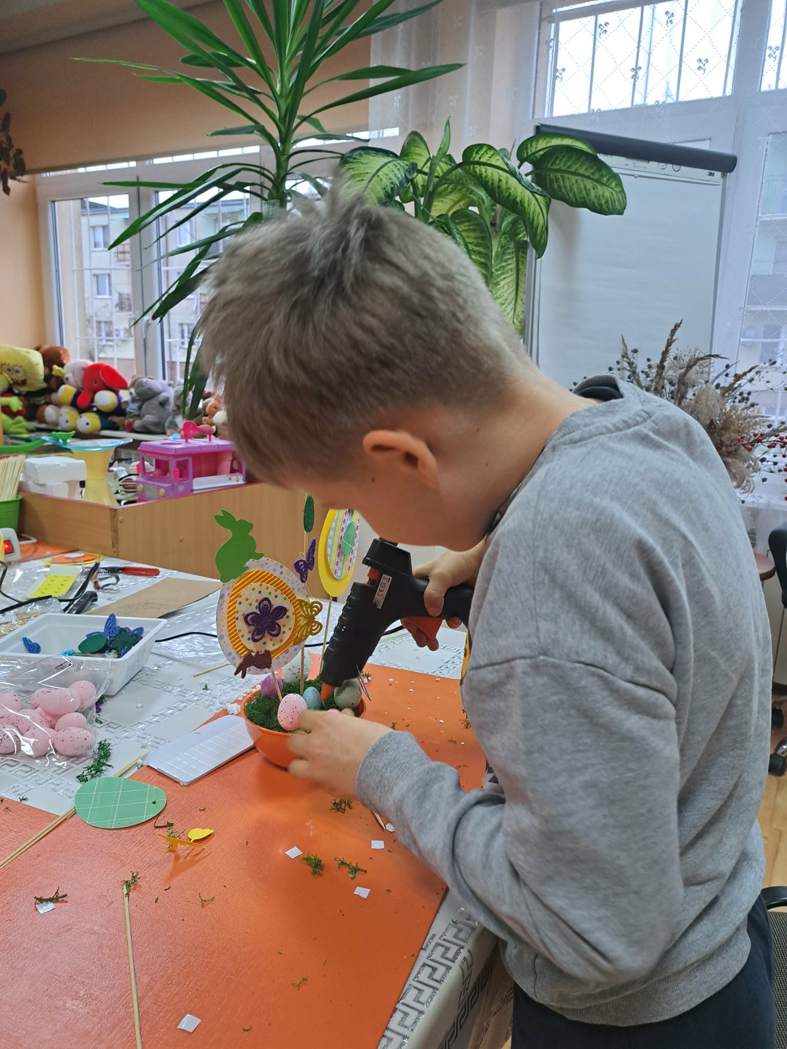 Chłopiec wykonuje świąteczny stroik, trzyma pistolet do kleju na gorąco.