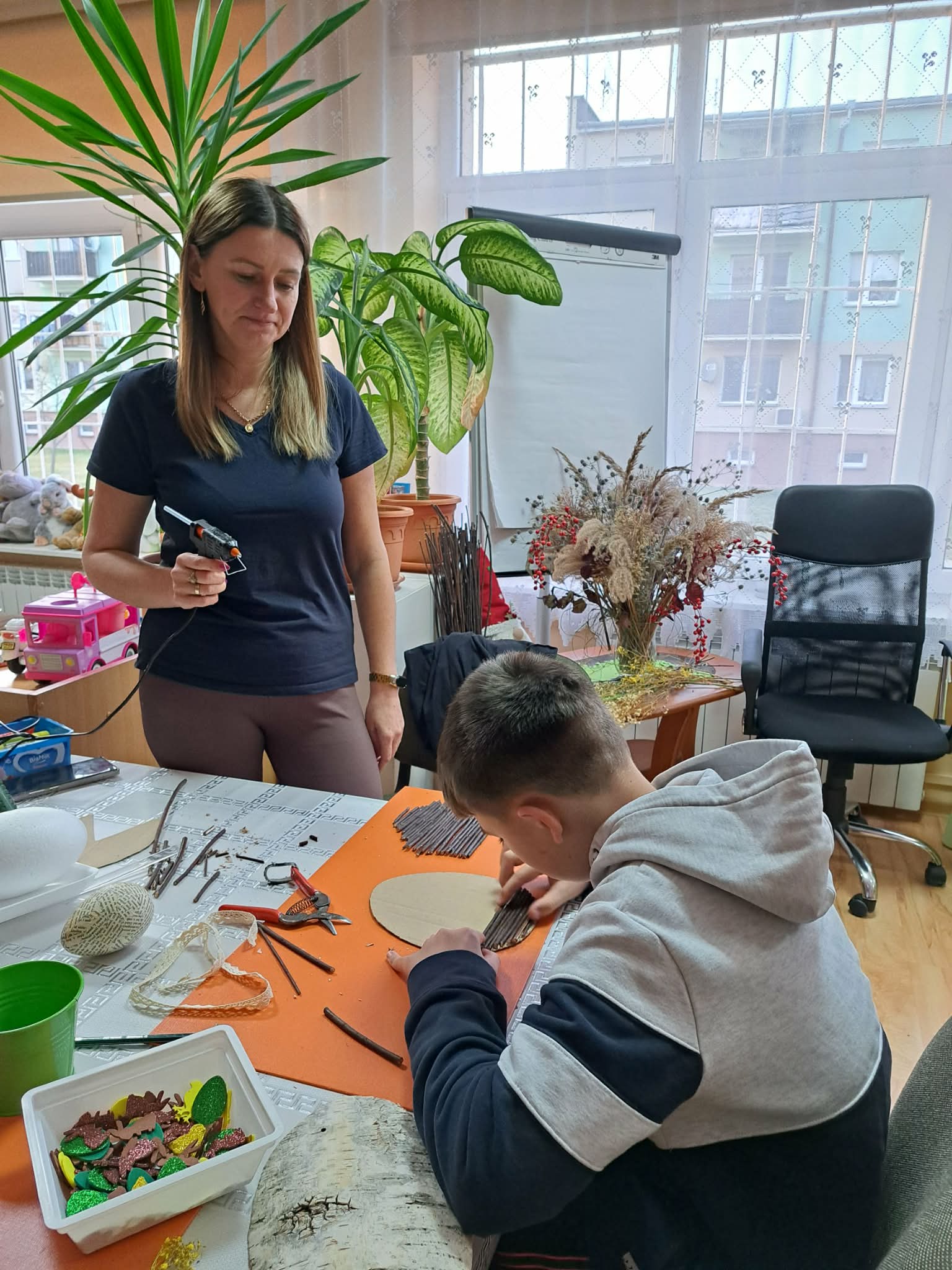 Kobieta stoi z pistoletem na klej na gorąco przy stole.