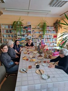 Panie siedzą przy wspólnym stole, zastawionym wielkanocnymi potrawami.